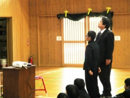 スーツを着た大人と制服姿の児童が並んで立っている写真