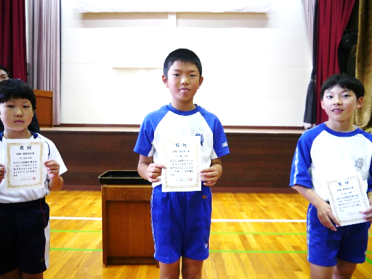 計算大会4回連続満点賞の3人が賞状を持って並んでいる写真