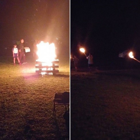 キャンプファイヤーや持っている松明が燃えているのを眺めている児童たちの写真