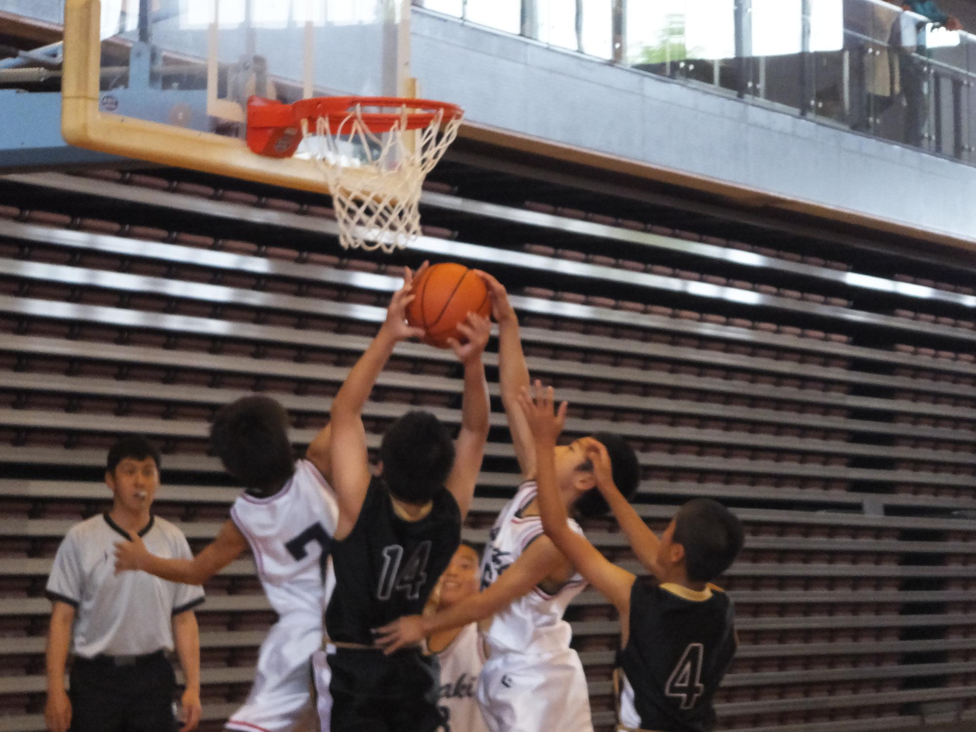 体育館のゴール下でユニフォーム姿の児童がボールを取り合っている写真