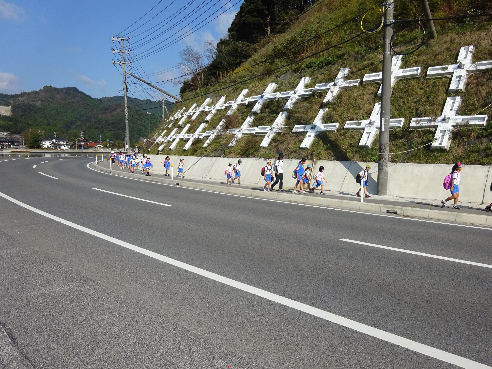 児童が歩道を列になって道路沿いを歩いている写真