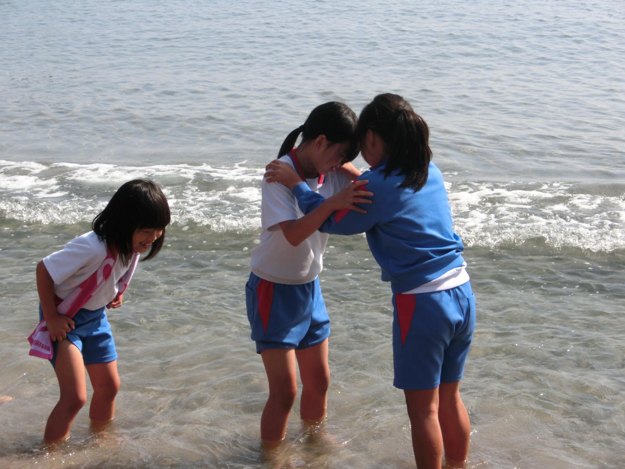 3人の女子児童が波打ち際で足を浸しながら遊んでいる写真