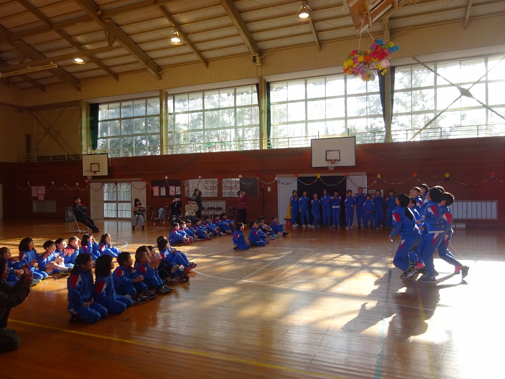 体育館で運動着姿の児童たちが天井の割れたくす玉に駆け寄っている写真