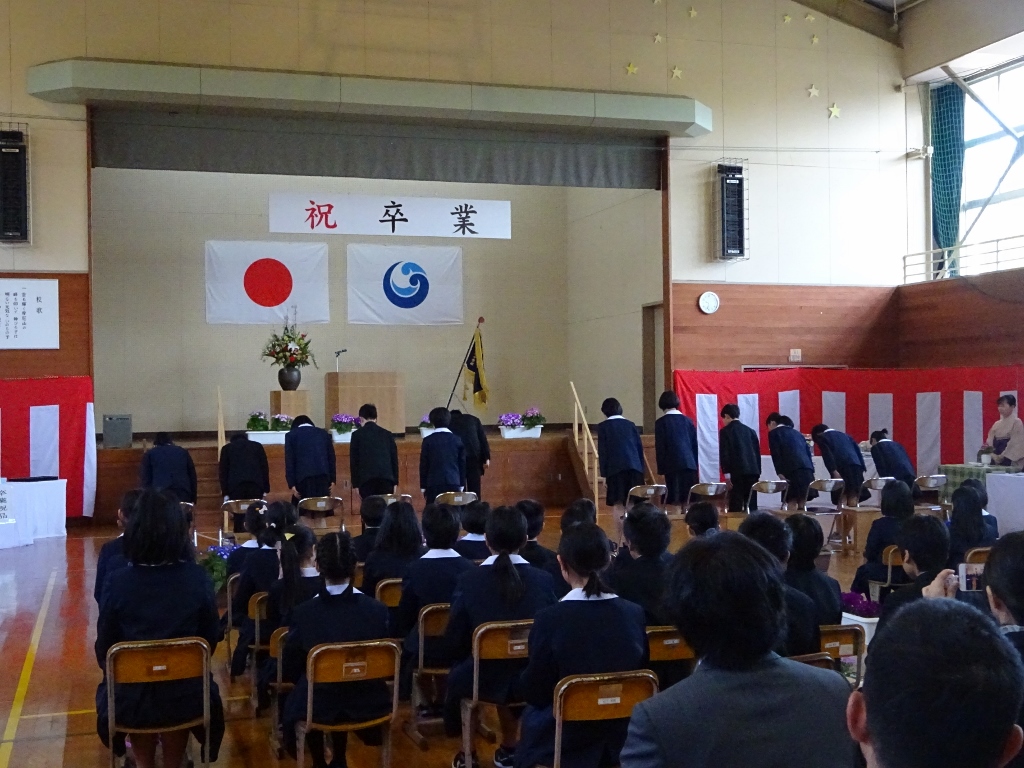 卒業生たちが体育館のステージに向かってお辞儀をしている写真