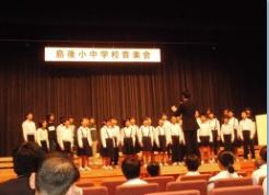 舞台で児童たちが指揮者の前で合唱している写真