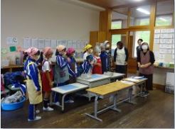 調理室で児童たちが指導者の話を聞いている写真