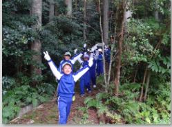 秋の遠足で林の中を列になって歩きピースをしている児童たちの写真