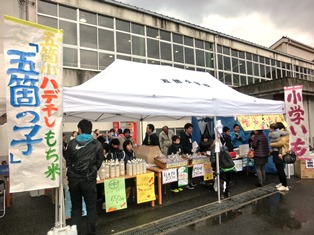 建物前に設置されたテントに複数の児童が商品を並べて販売している写真