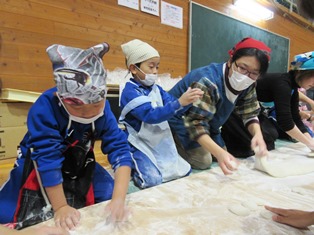 エプロンと三角巾を着けた児童や大人が餅を丸めている写真