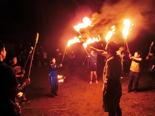 屋外の暗い場所で、人々が手に持ったたいまつを高く掲げて立っている写真