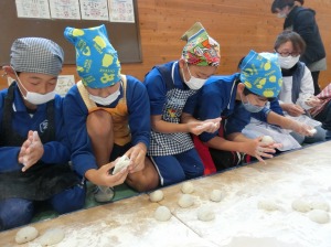 三角巾を頭に身に着けた複数の児童が餅を丸めている写真