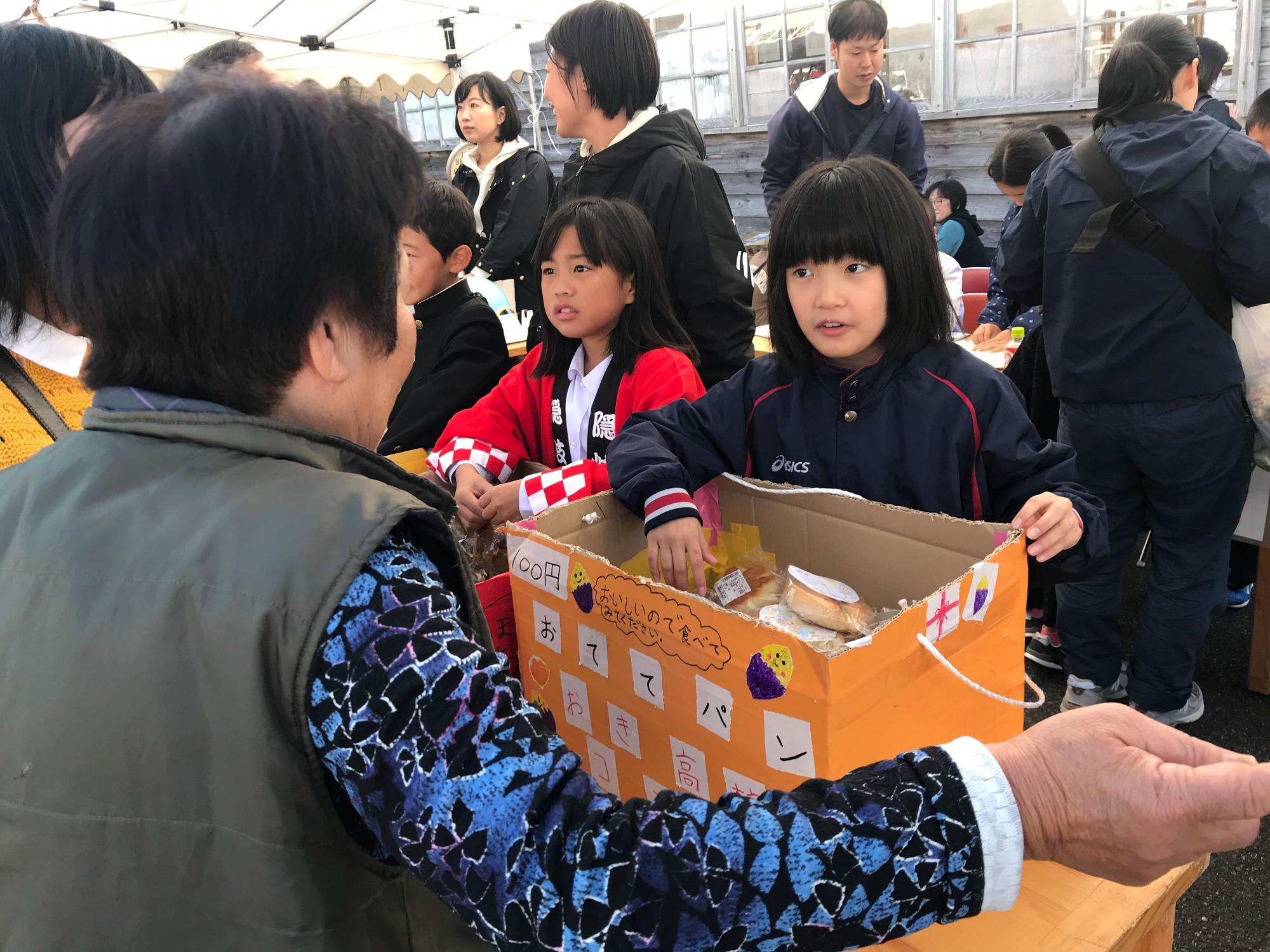 児童が段ボールに入った品物を渡しながら女性と話している写真