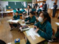 着席して授業を受ける児童たちを先生たちが参観している写真