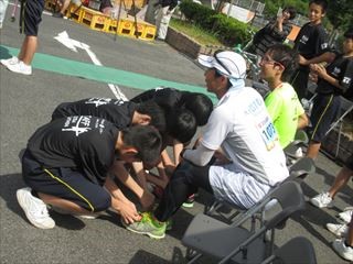 椅子に座るランナーの靴ひもを結ぶ生徒たちの写真