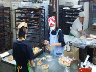 エプロンと三角巾姿の生徒たちがパンを袋詰めしている写真