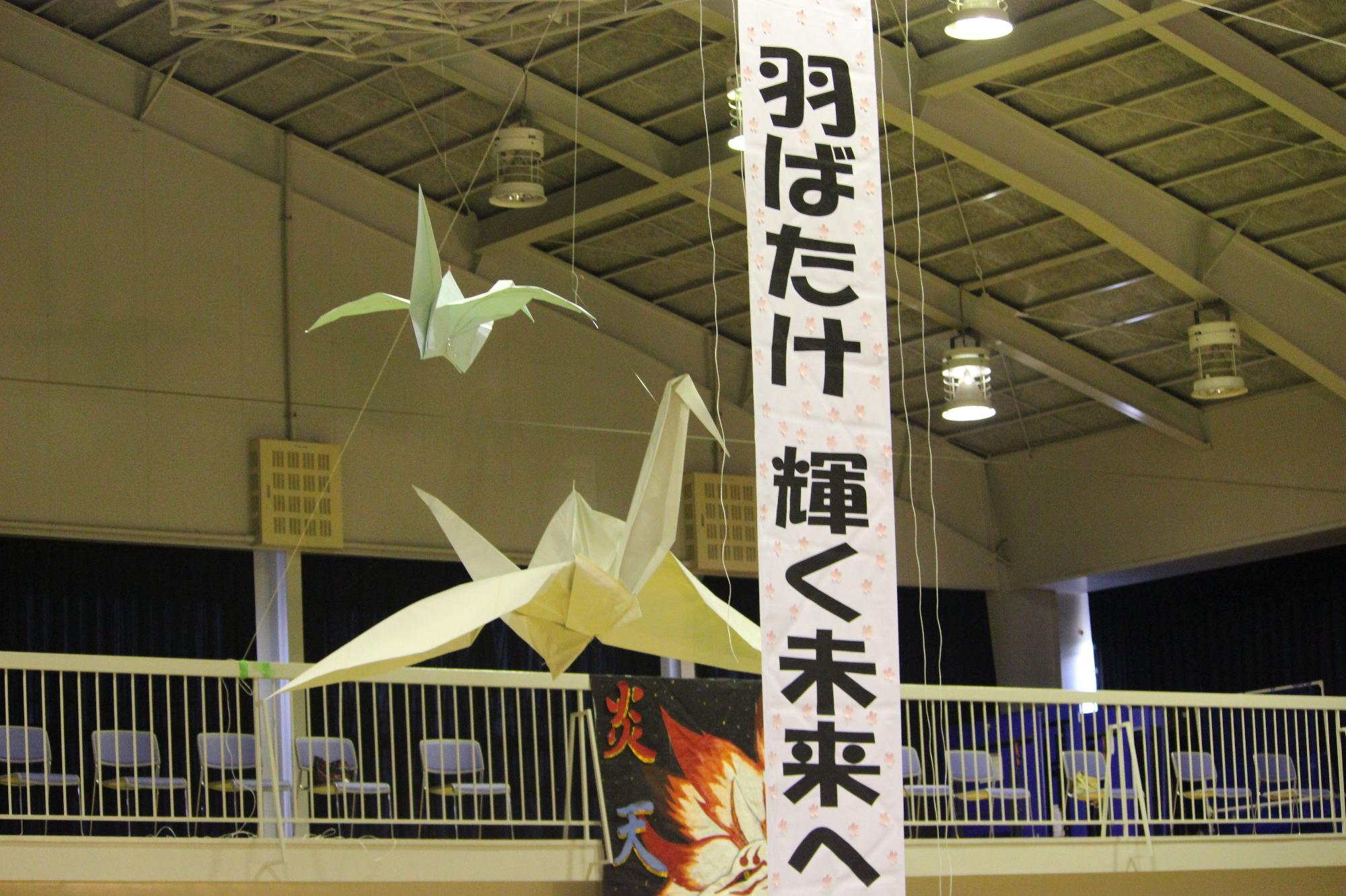 体育館に大きな折り鶴と標語の垂れ幕が掲げられている写真