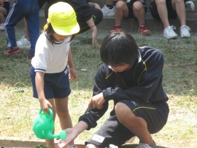 生徒が見守り園児と一緒に水やりを手伝っている写真