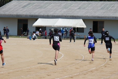 ゼッケンを付けた走者が競技場を全力で走っている写真