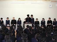 壇上で生徒が前に立ち年頭所感を発表し、他の生徒が座って見守っている写真