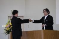 壇上で先生から男子生徒が書類を受け取り握手している写真