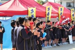 屋外で多くの生徒が並び、声援用の道具を手に応援している写真