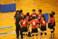 体育館で背番号のバレーボールの選手たちが円になり監督の指示を聞いている写真