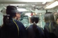 狭い船内で子どもたちが機械の説明を受けている写真