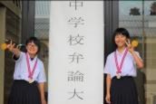 中学校弁論大会と書かれた看板の前に二人の生徒が立ち、ピースをしている写真