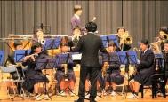 舞台上で、生徒たちが指揮に合わせて管楽器や打楽器を演奏している写真