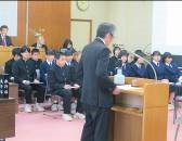 壇上で大人が話し、生徒が着席して聞いている写真