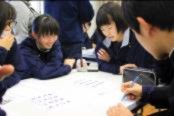 生徒たちが机を囲みプリントを見ながら話し合っている写真