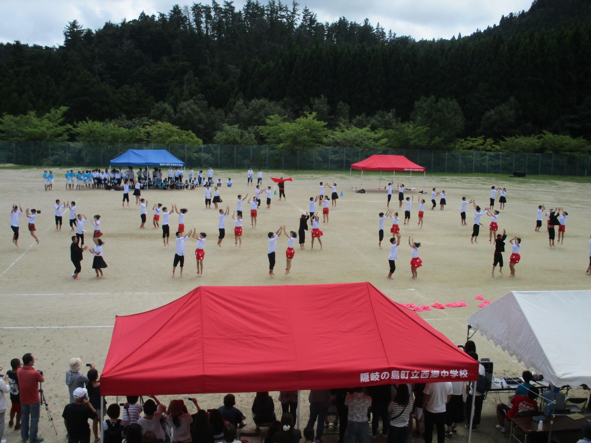 校庭で生徒たちが2人1組になり手を合わせながら踊っている写真