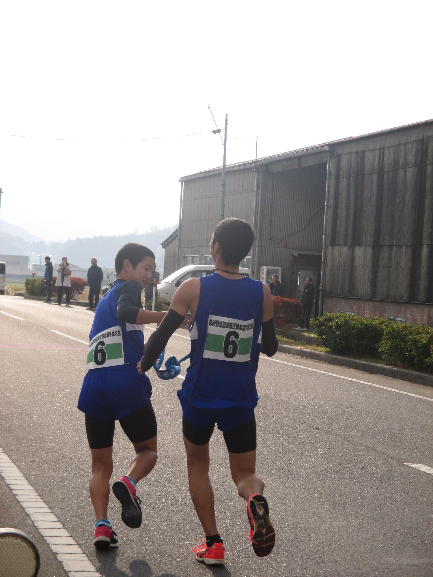 ユニフォーム姿の生徒が襷をもう1人の走者に受け渡している写真