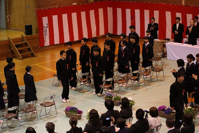 体育館のフロアに卒業生たちが起立している写真