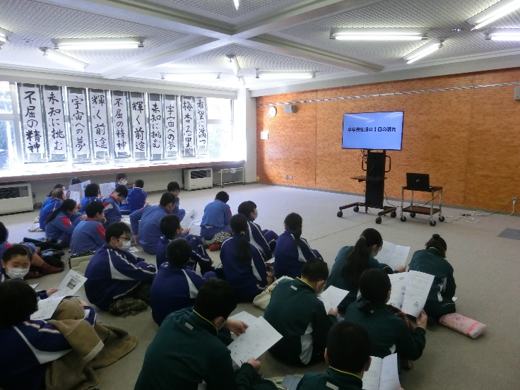 床に座った6年生が前方のモニターを見ている写真