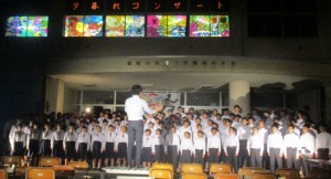 校舎前に多くの生徒が並び、指揮者に合わせて合唱している写真