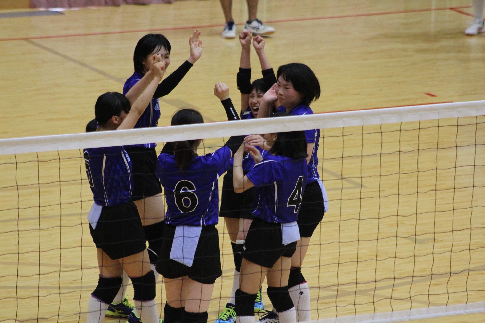 女子選手がバレーボールのコートで円になっている写真