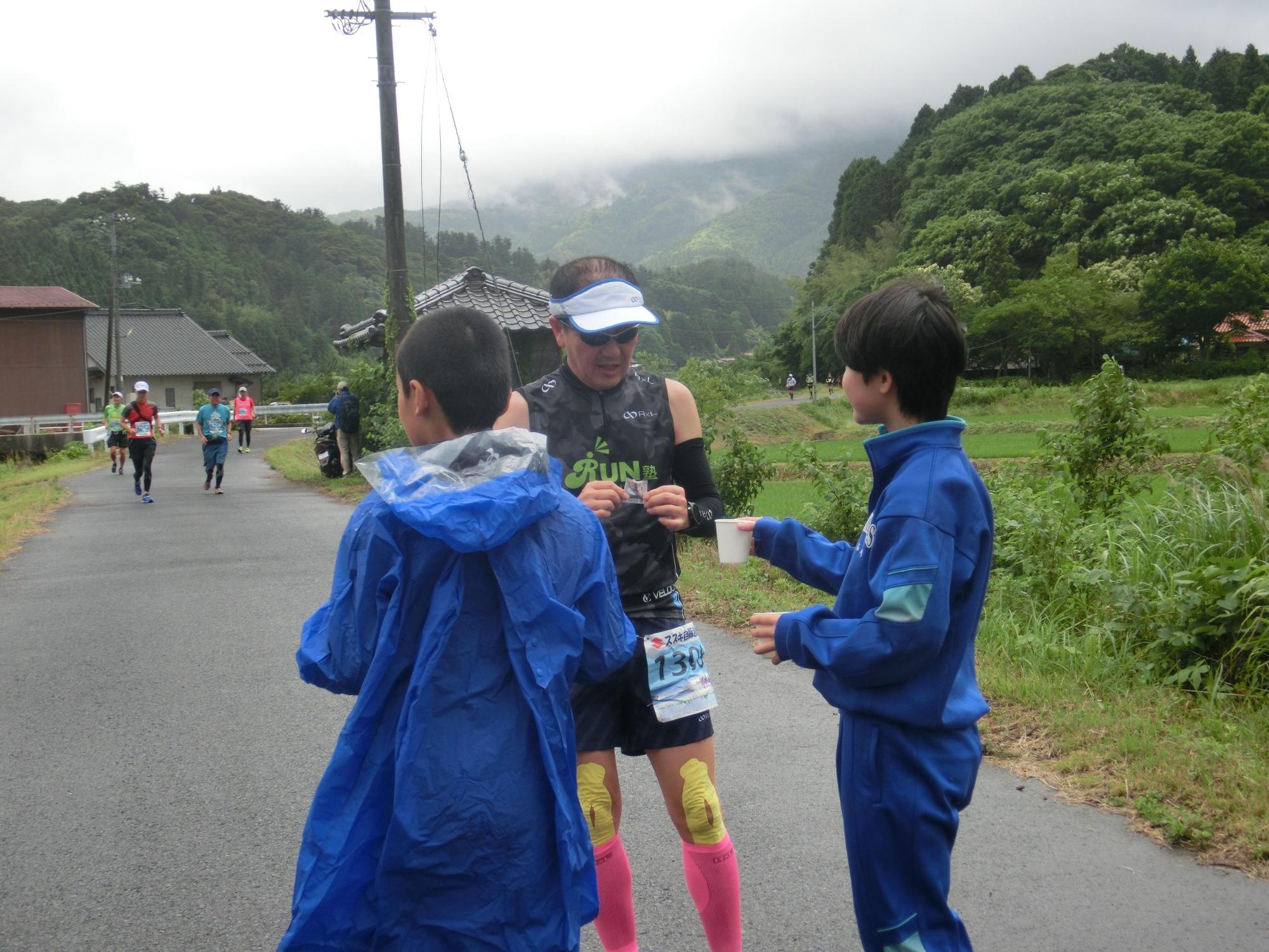 マラソンランナーに紙コップを渡している生徒の写真