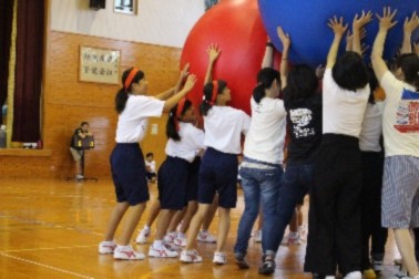複数の大きな球体を大勢の生徒が持ち上げる競技をしている写真