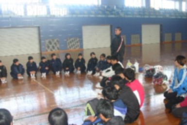 体育館のフロアに輪になって座って話を聞いている生徒たちの写真