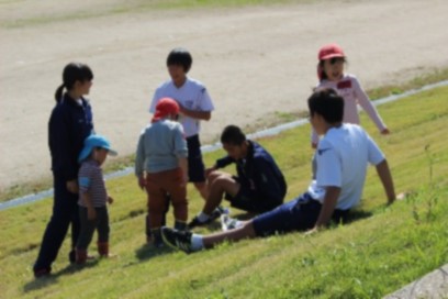 草の生えた土手でくつろぐ保育園児と生徒たちの写真