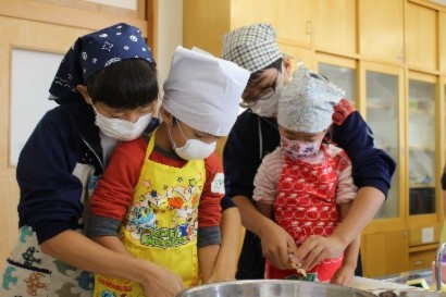 調理をしている保育園児を後ろから手助けしている生徒の写真