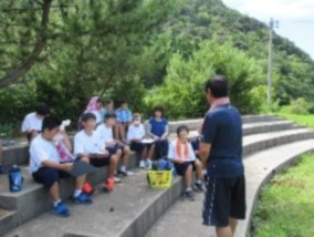 コンクリートの石段に座って話を聞いている生徒たちの写真