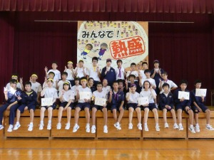 体育館のステージ上で「みんなで！熱盛」と書かれたスローガンをバックに生徒達が賞状を手に持ちポーズをとっている写真