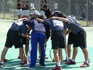 テニスコートで生徒達が円になりラケットを手に持ち肩を組んでいる写真