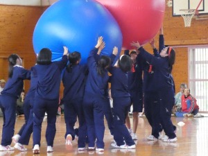 体育館で複数の生徒達が二つの大きな玉を押し合って競い合っている写真