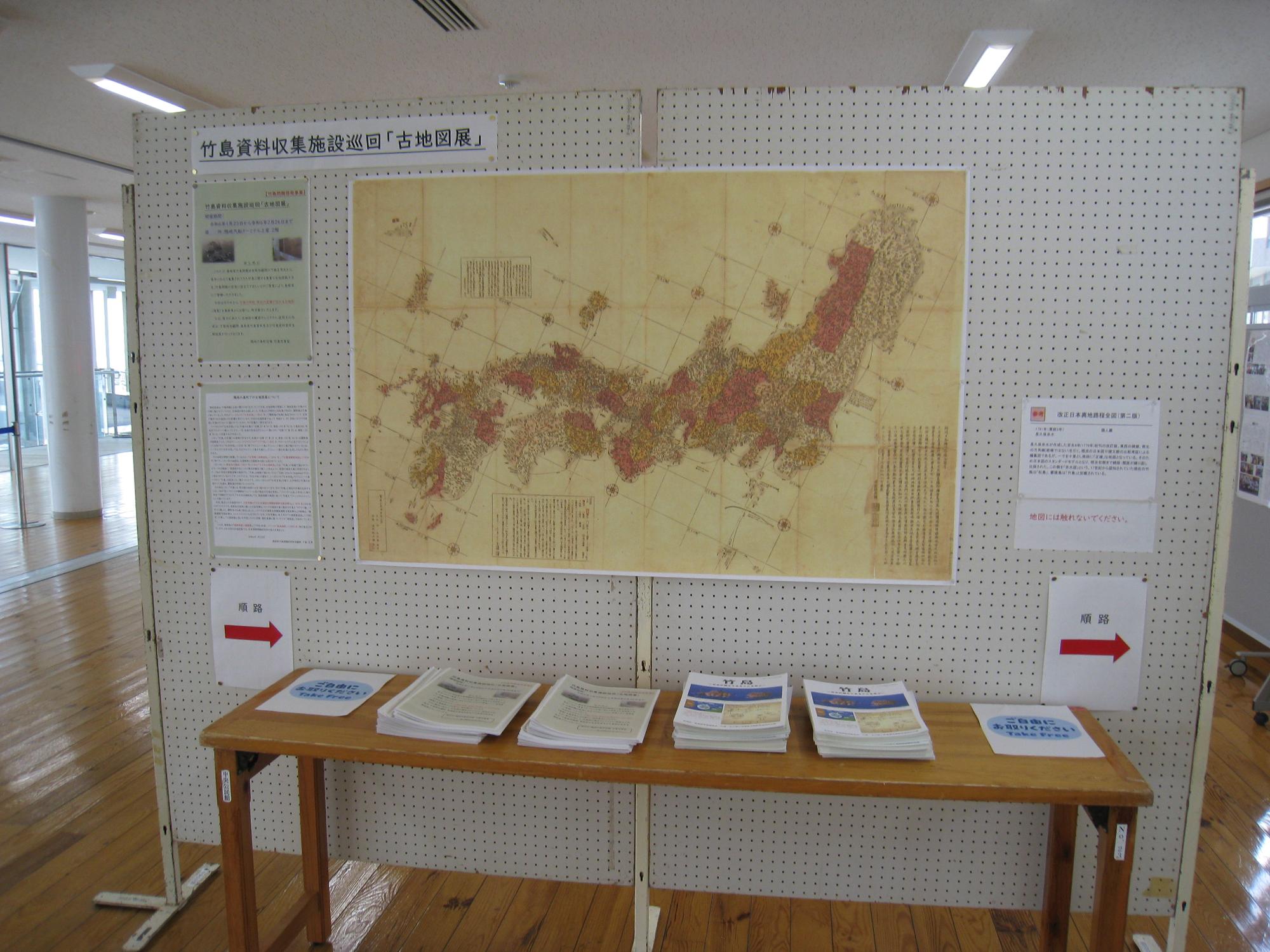 古地図展に展示されている日本地図の写真。手前にはパンフレットなどが並んでいる。