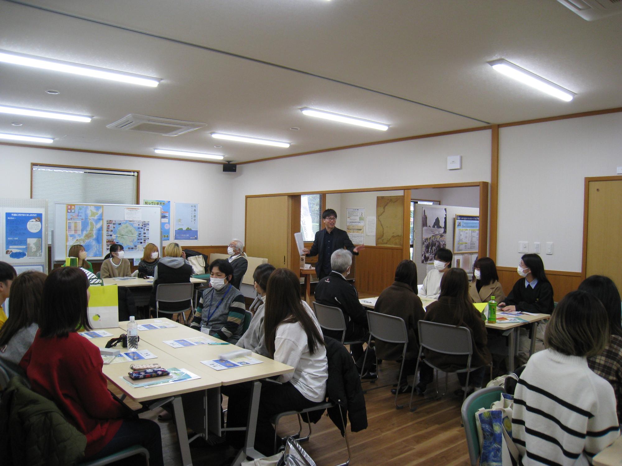 久見区長や竹島資料収集施設管理人が学生たちにインタビュー調査をしている写真