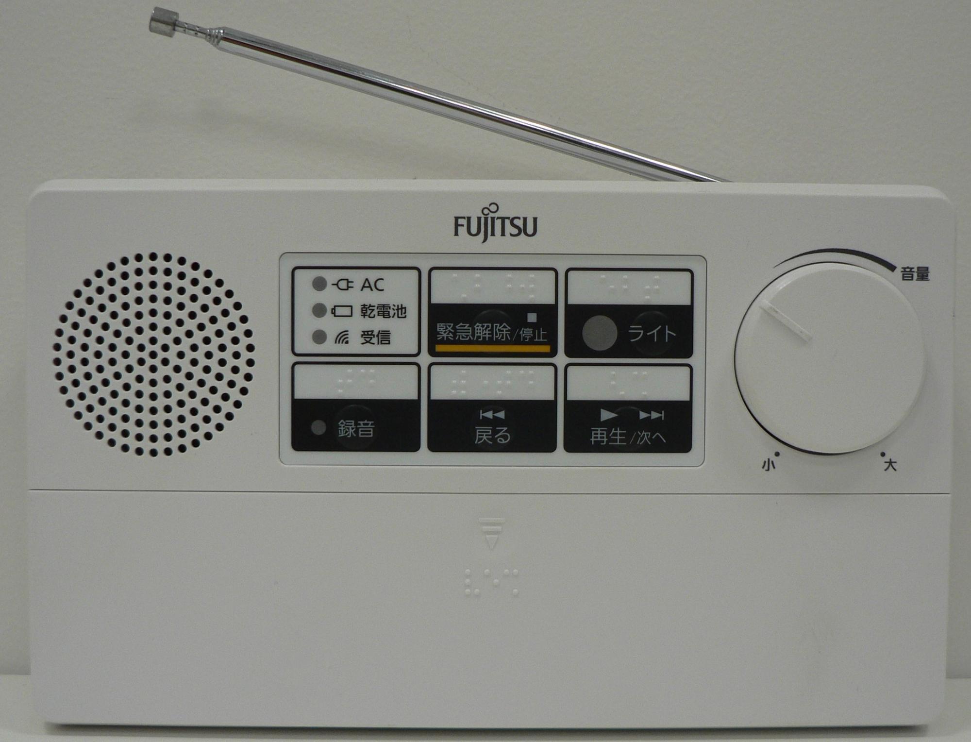 白い筐体の前面に操作パネル、スピーカーの穴、ボリュームのダイヤルがあり、上側にアンテナが伸びている富士通製の防災行政無線受信機「CR-672B型」の写真